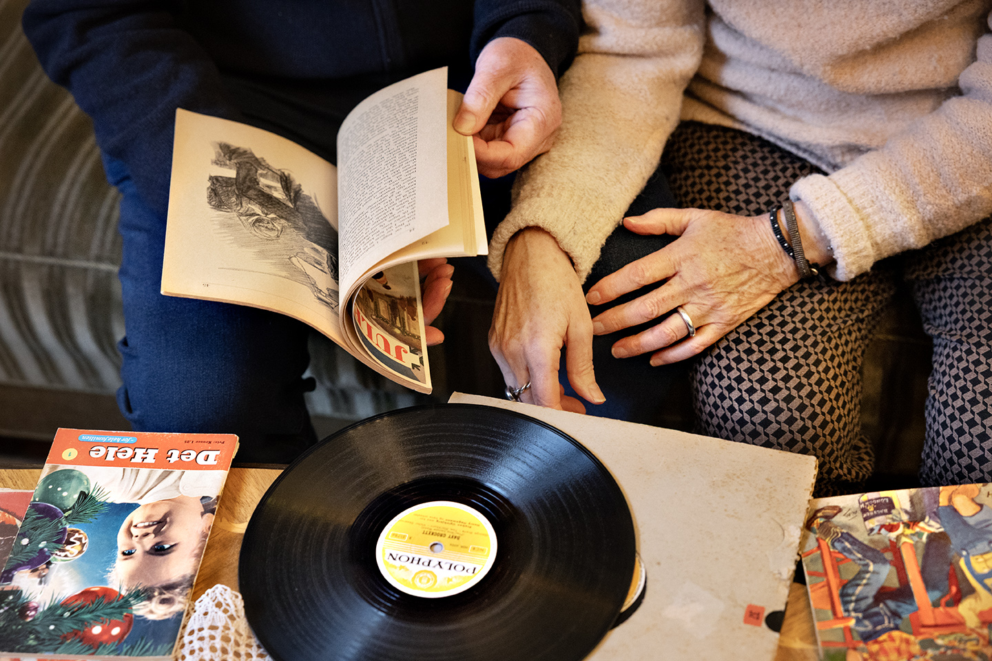To personer bladrer i gamle magasiner fra Erindringslejligheden i Den Gamle By. Der er også en vinylplade.