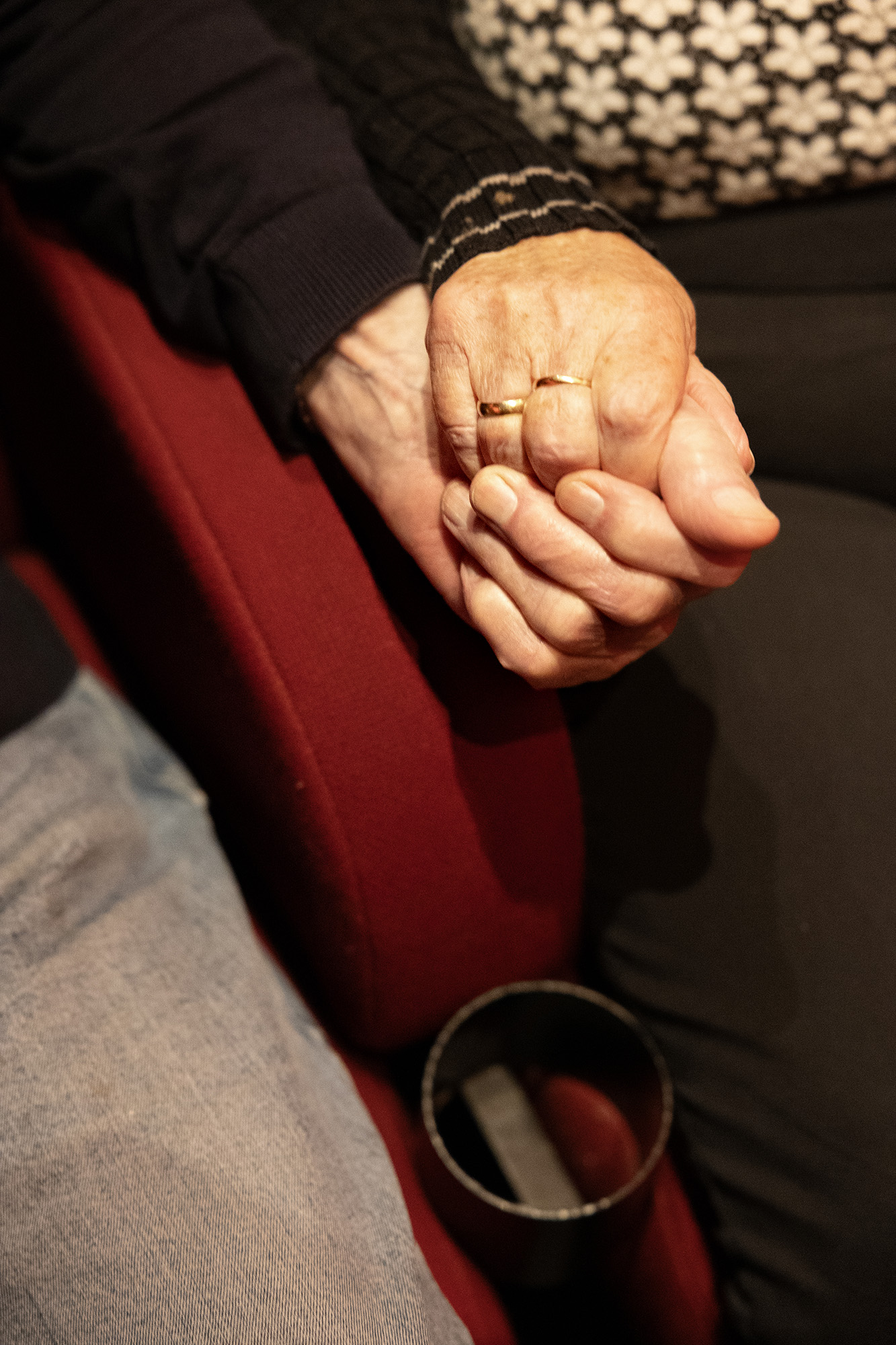En mand og en kvinde knytter hænder i biografsalen. Man kan se vielsesringen på kvindens finger.