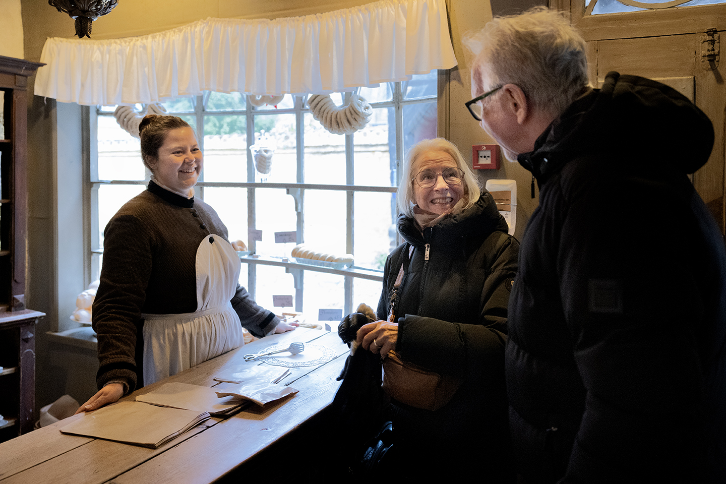 Ægteparret er på besøg i en af butikkerne i Den Gamle By, hvor de snakker med en ansat i forretningen.
